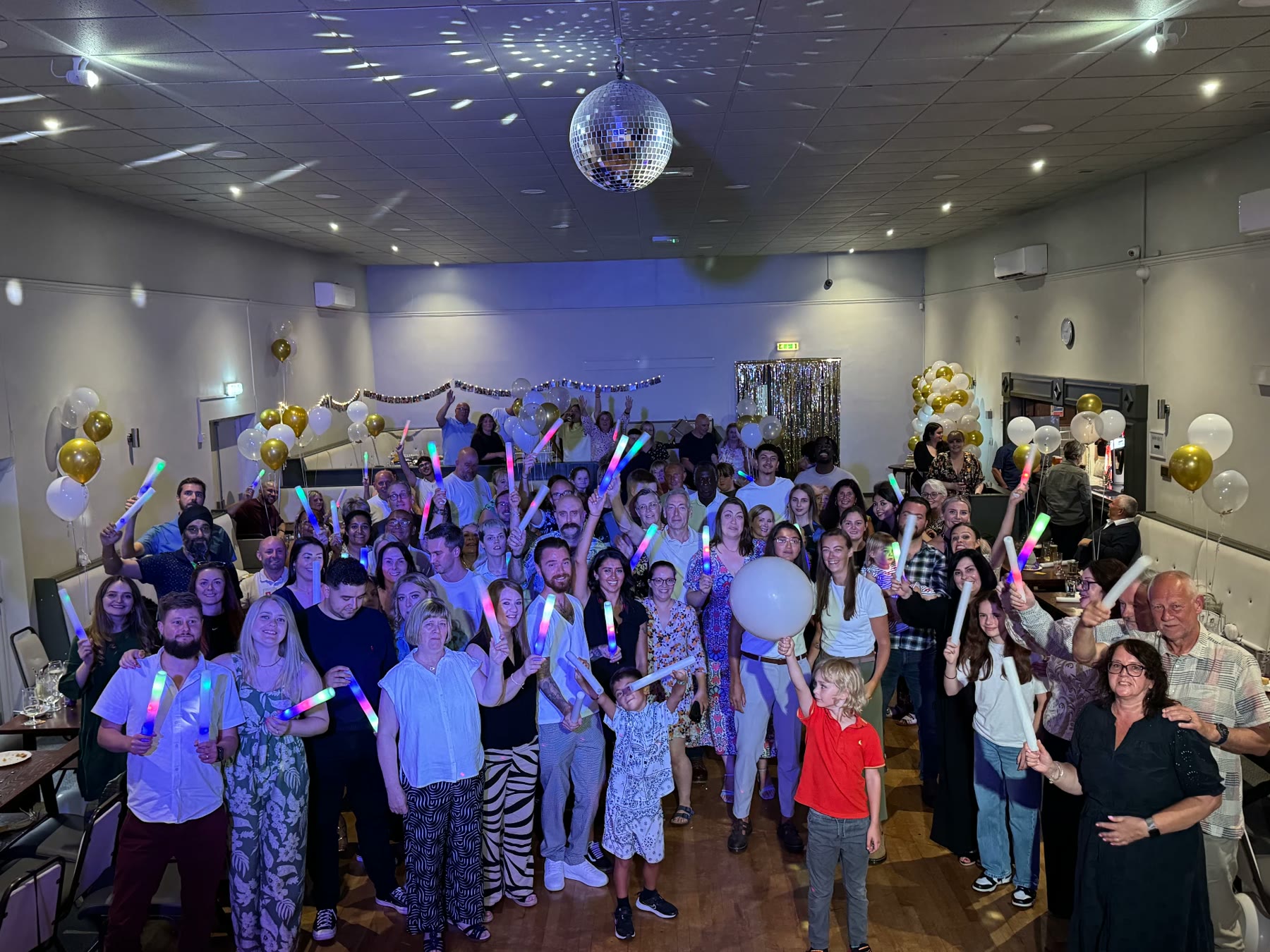 Packed party crowd holding glow sticks under a mirror ball and blue lighting