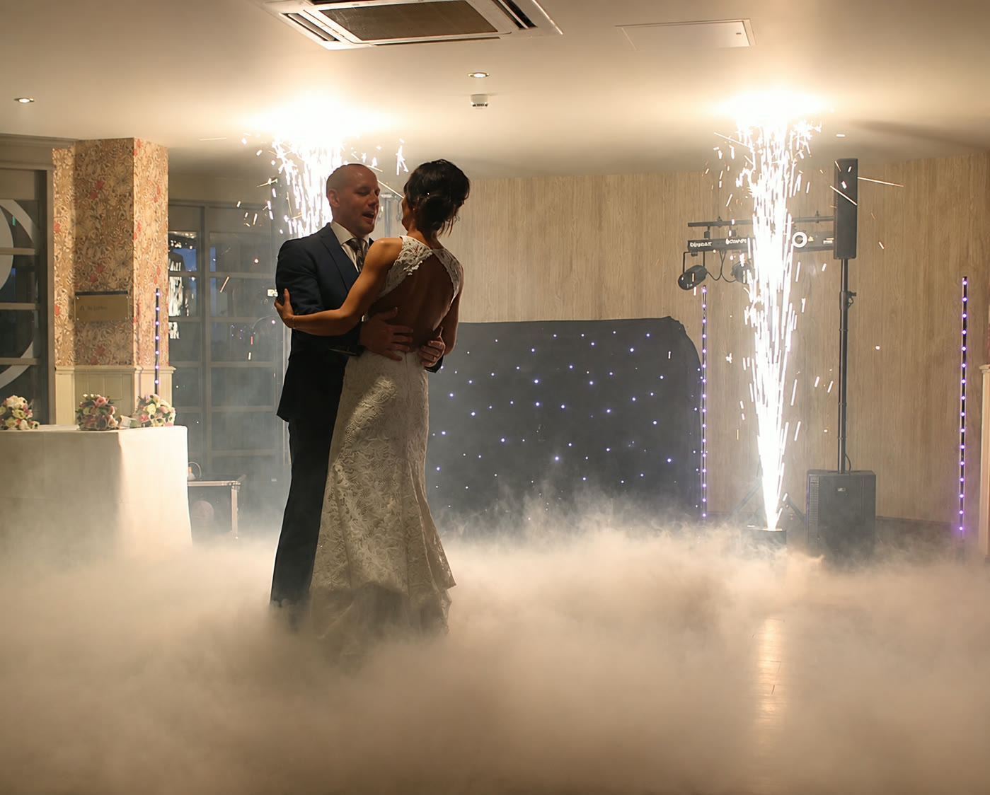 Bride and groom's first dance in thick low fog with cold spark fountains behind them