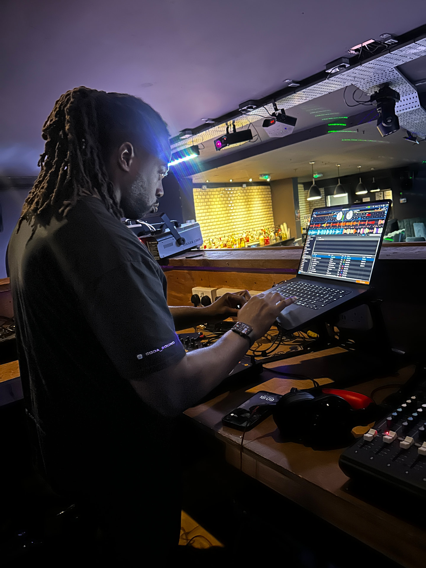 DJ Coda mixing at a venue bar with disco lighting and laptop