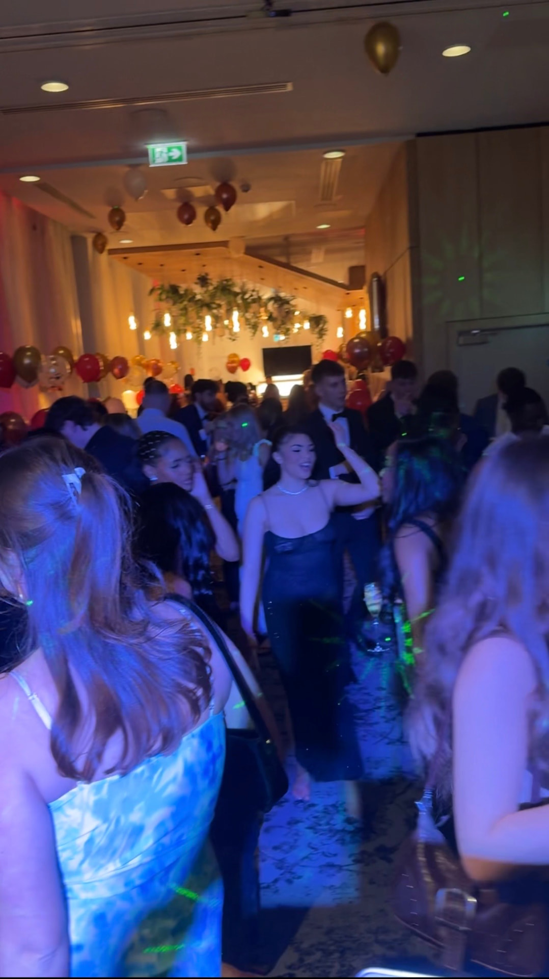 Packed dancefloor at a party with blue lighting and balloon decor